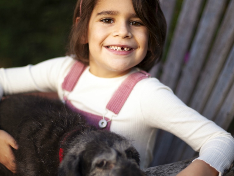 A smiling child sitting on a porch with a dog on their lap
