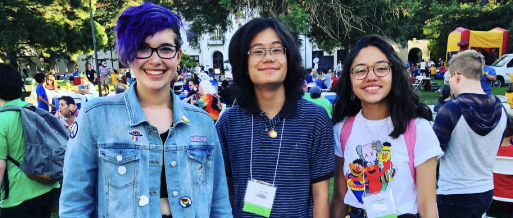 Three teenagers smiling together at an outdoor gathering