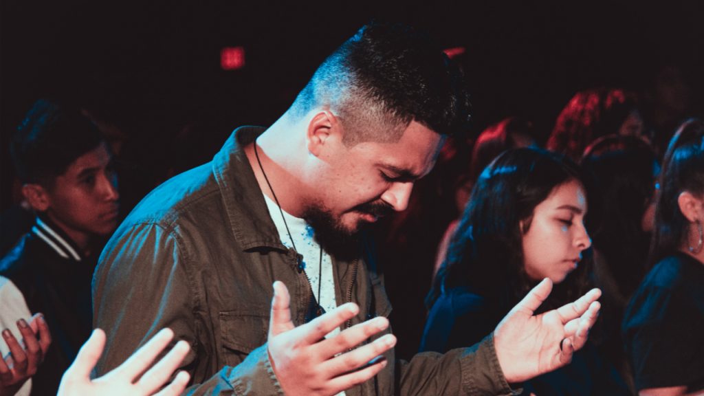 A man with raised hands during a worship service, young people nearby